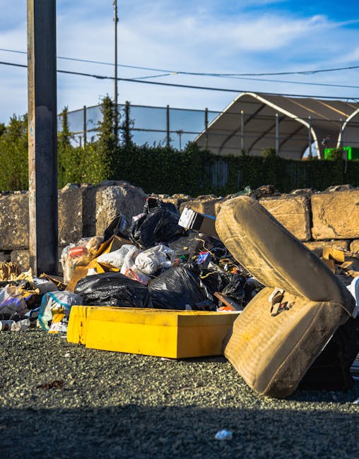 In the image, a large pile of mixed waste is displayed on a paved driveway area, situated outdoors near a building with a brick wall and a window. The rubbish consists of various materials, including 